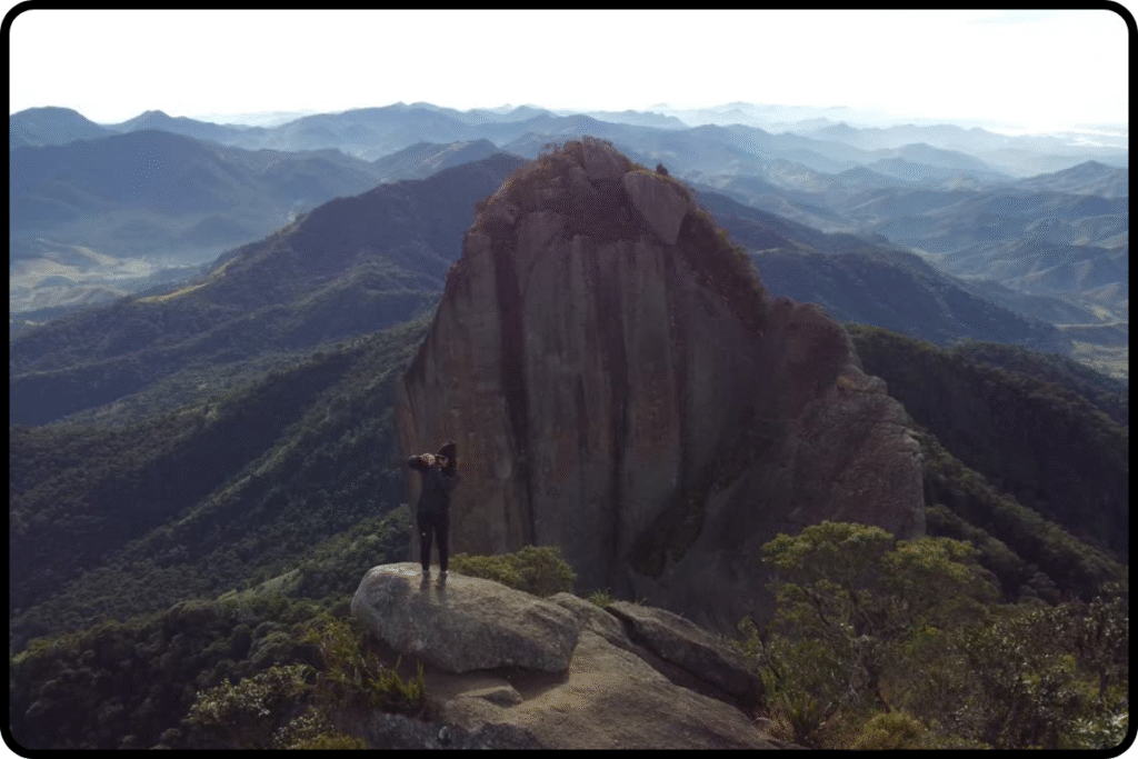 Vista aérea da trilha da Pedra Selada com luz suave do amanhecer, destacando o cume rochoso em meio à Serra da Mantiqueira