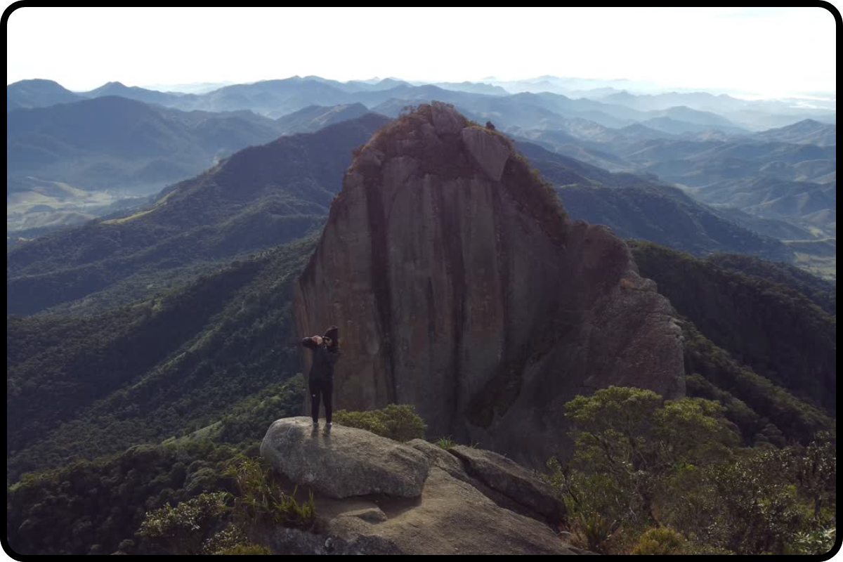 Vista aérea da trilha da Pedra Selada com luz suave do amanhecer, destacando o cume rochoso em meio à Serra da Mantiqueira