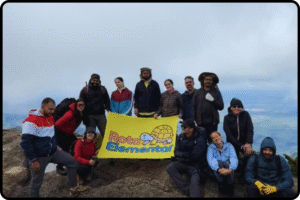 Grupo de trilheiros no cume do Pico dos Marins segurando bandeira da Rota Elemetar após conquistar os 2.420 metros