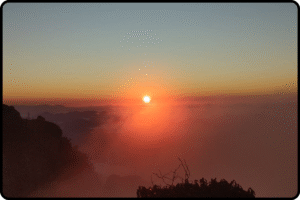 Nascer do sol visto do alto da Pedra Selada, com o céu tingido de tons alaranjados sobre a Serra da Mantiqueira