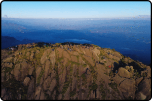 Vista do cume com dimensão da Altura do Pico dos Marins ao amanhecer, com rochas douradas e céu azul profundo