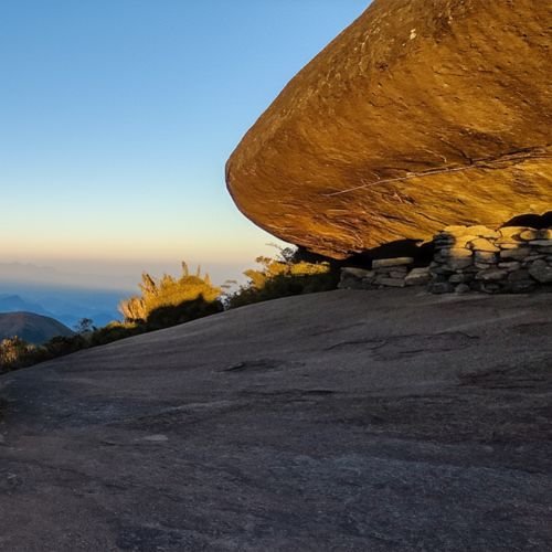 Imensa rocha suspensa do Castelo do Açu com área de acampamento de montanha sob a luz suave do fim de tarde na Travessia Petrópolis Teresópolis.