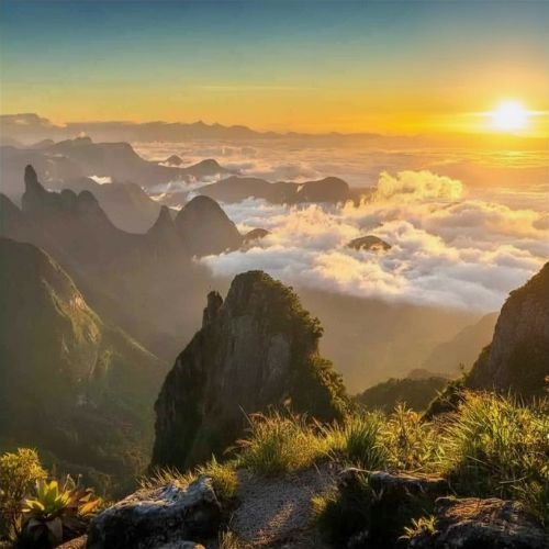 Nascer do sol iluminando as nuvens baixas e os picos de pedra nos Portais de Hércules durante a Travessia Petrópolis Teresópolis da Rota Elementar no PARNASO.