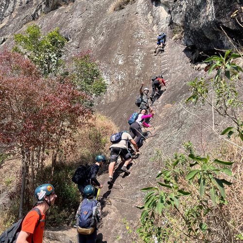 A subida pela face norte ou face sul da Pedra do Baú não se resume a uma caminhada convencional; trata-se de uma rota clássica de via ferrata que impõe respeito e exige estabilidade emocional diante da altura exposta. O percurso apresenta trechos íngremes de rocha nua e centenas de degraus que formam a icônica escada de ferro, demandando o uso correto de técnicas de ancoragem contínua e autoseguro. Para quem busca evoluir do trekking básico para o montanhismo técnico, este roteiro em São Bento do Sapucaí funciona como a introdução perfeita, desde que amparado por uma equipe profissional capaz de gerenciar a exposição e a verticalidade do paredão.Na Rota Elementar, nós eliminamos as principais objeções técnicas e logísticas para que você foque totalmente na sua linha de progressão. Nossa metodologia de campo foca na gestão de ritmo do grupo:Treinamento na Base: Antes de tocar no primeiro degrau da escada de ferro, realizamos uma instrução prática obrigatória sobre o manuseio dos mosquetões e o posicionamento correto dos pés.Equipamentos Inclusos: Não há necessidade de aluguel externo; entregamos capacetes e sistemas de segurança revisados e em total conformidade com as normas internacionais de via ferrata.Liderança de Campo: Nossos guias regulam a velocidade da subida para evitar o desgaste físico prematuro, garantindo o aproveitamento consciente e seguro de todos os degraus até o cume.
