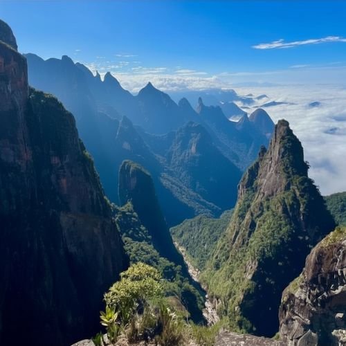 Vale profundo cercado por imensos paredões de pedra verticais sob céu azul com nuvens na rota de trekking da Travessia Petrópolis Teresópolis.
