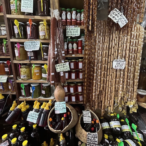 Prateleiras com produtos artesanais, conservas e bebidas típicas da cultura regional brasileira.