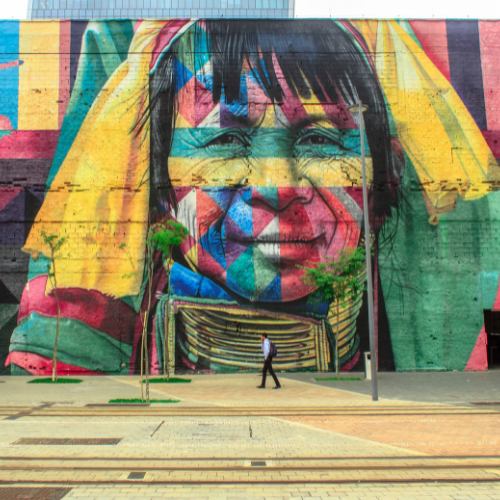 Mural de arte urbana colorida representando um rosto indígena em estilo mosaico.
